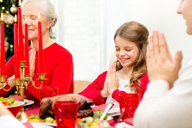 concepto de familia, vacaciones, generación, navidad y personas - familia sonriente cenando y rezando en casa