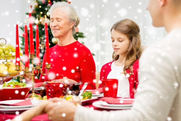 concepto de familia, vacaciones, generación, navidad y personas - familia sonriente cenando y rezando en casa