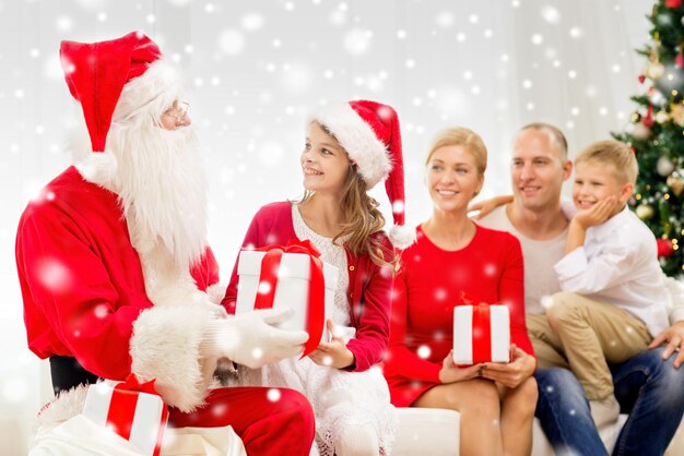 concepto de familia, vacaciones, generación, navidad y personas - familia sonriente con santa claus y cajas de regalo en casa