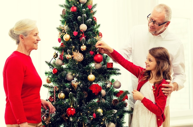 concepto de familia, vacaciones, generación y personas - familia sonriente decorando el árbol de Navidad en casa