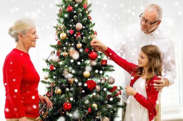 concepto de familia, vacaciones, generación y personas - familia sonriente decorando el árbol de Navidad en casa