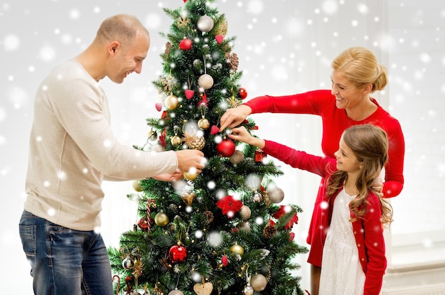 concepto de familia, vacaciones, generación y personas - familia sonriente decorando el árbol de Navidad en casa