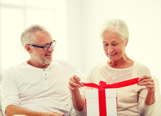 concepto de familia, vacaciones, Navidad, edad y personas - feliz pareja de ancianos con caja de regalo sobre fondo de habitación blanca