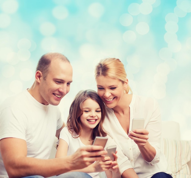 concepto de familia, vacaciones, tecnología y personas: madre, padre y niña sonrientes con smartphones sobre fondo de luces azules