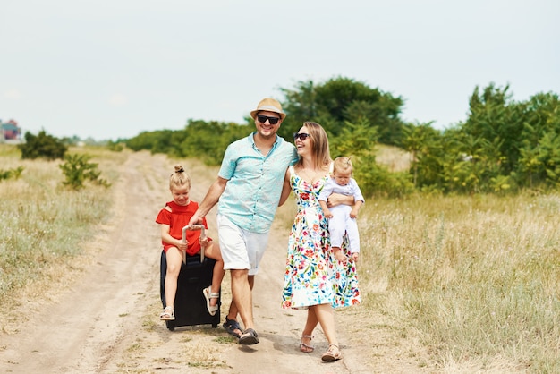 Concepto de familia, vacaciones de verano, adopción y personas: hombre feliz, mujer e hijas en gafas de sol, con maletas divirtiéndose sobre el cielo azul