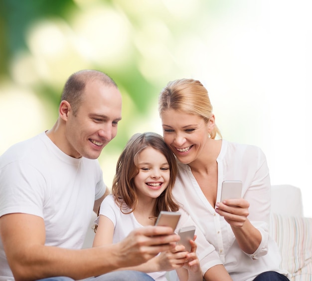 concepto de familia, verano, tecnología y personas: madre, padre y niña sonrientes con smartphones sobre fondo verde