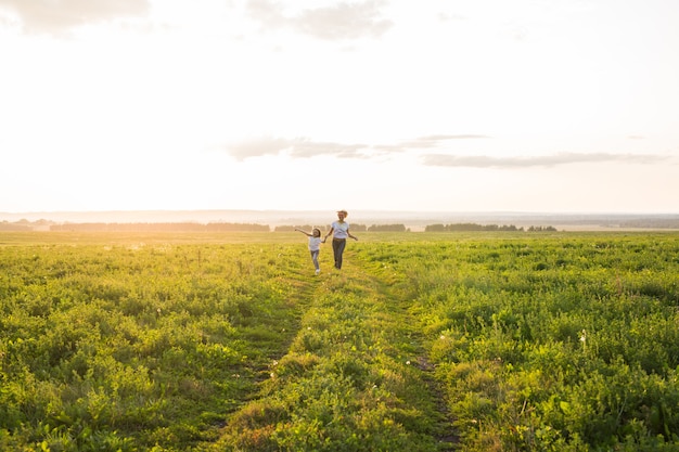 Concepto de familia, verano y vacaciones - pequeña hija y madre corren en el campo de verano.