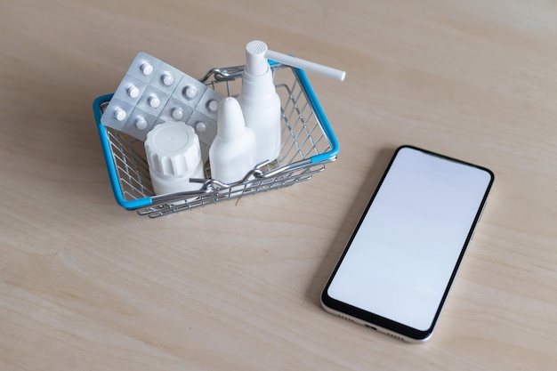 Concepto de farmacia en línea con entrega a domicilio Compra de medicamentos en línea por teléfono Mini carro con diferentes tabletas aerosoles cápsulas y un teléfono inteligente con una pantalla en blanco Flecha hecha de pastillas