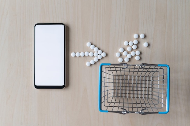 Concepto de farmacia en línea con entrega a domicilio Compra de medicamentos en línea por teléfono Mini carro con diferentes tabletas aerosoles cápsulas y un teléfono inteligente con una pantalla en blanco Flecha hecha de pastillas