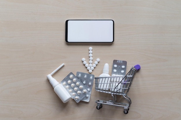 Concepto de farmacia en línea con entrega a domicilio Compra de medicamentos en línea por teléfono Mini carro con diferentes tabletas aerosoles cápsulas y un teléfono inteligente con una pantalla en blanco Flecha hecha de pastillas