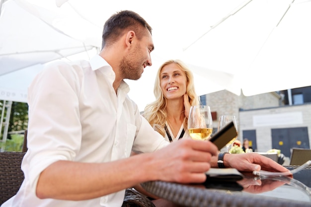 concepto de fecha, personas, pago y finanzas - pareja feliz con tarjeta de crédito y copas de vino pagando la cuenta en el restaurante