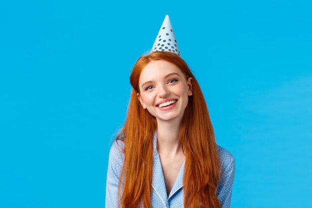 Concepto de felicidad, belleza y celebración. Alegre pelirroja despreocupada mujer b-day hat