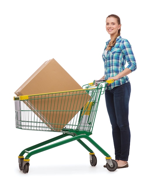 concepto de felicidad, compras y personas - mujer joven sonriente con carrito de compras y caja grande en él