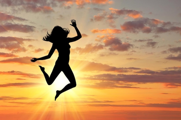 Concepto de felicidad y libertad. Silueta de mujer feliz saltando al atardecer