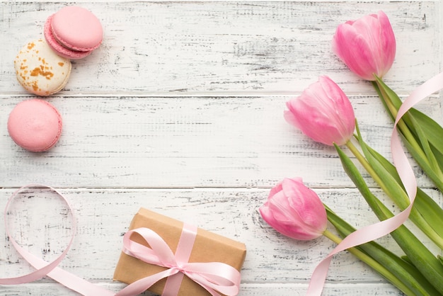 Concepto de feliz cumpleaños. Vista superior de la foto plana de hermosas flores envueltas en una caja de regalo de papel y tres sabrosos y deliciosos macarrones en una mesa de madera vintage