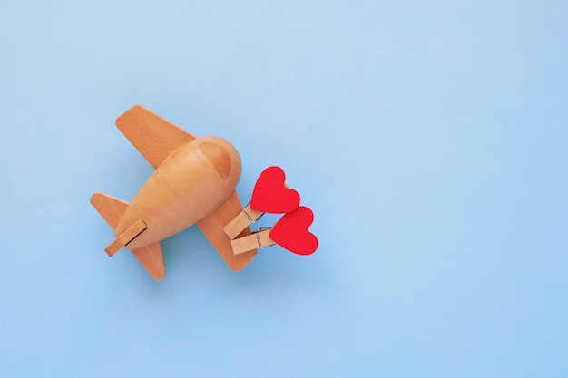 Foto concepto de feliz día de san valentín. avión infantil de madera ecológica sobre un fondo azul con corazón rojo.