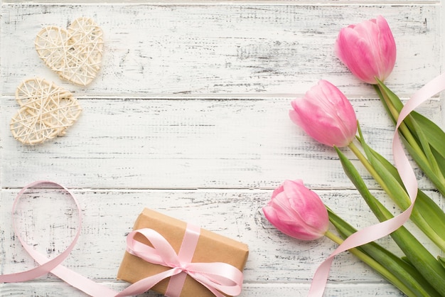 Concepto de feliz día de San Valentín. Foto de composición de primer plano sobre la cabeza plana de tulipanes pastel con tallos verdes paquete envuelto en papel kraft y corazones blancos en un escritorio vintage de madera