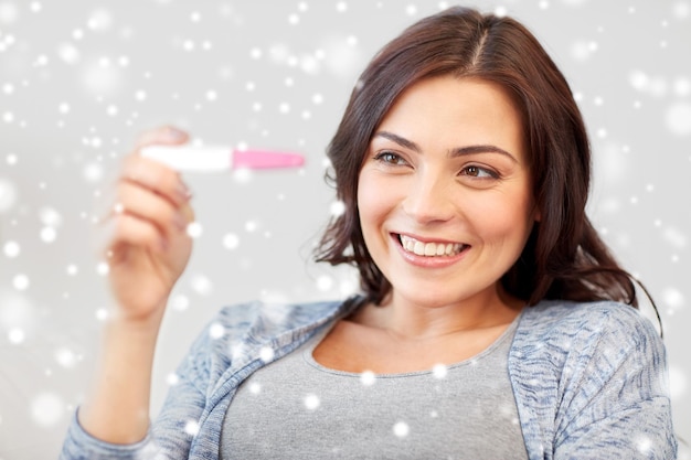 concepto de fertilidad, invierno, maternidad y personas - mujer sonriente feliz mirando la prueba de embarazo en casa sobre la nieve