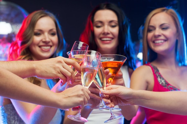Concepto de fiesta, celebración, amigos, despedida de soltera y cumpleaños: tres hermosas mujeres en vestidos de noche con cócteles y bola de discoteca
