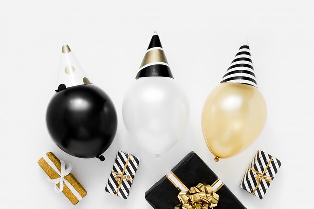 Concepto de fiesta de navidad. Globos blancos, negros y dorados en sombreros de fiesta sobre fondo blanco. Feliz año nuevo celebración