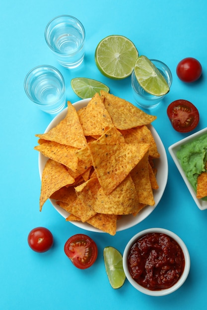 Concepto de fiesta con tequila, guacamole y patatas fritas sobre fondo azul.