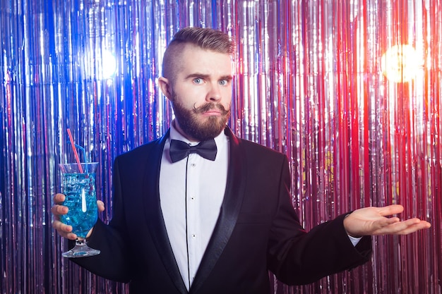 Foto concepto de fiesta y vacaciones de club - retrato de hombre guapo elegante con un traje caro tiene cóctel azul sobre fondo brillante.