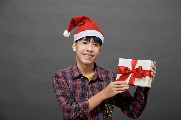 Concepto de fiesta y vacaciones de Navidad. Joven asiático con caja de regalo foto de estudio, aislado sobre fondo gris