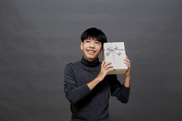 Concepto de fiesta y vacaciones de Navidad. Joven asiático con caja de regalo foto de estudio, aislado sobre fondo gris