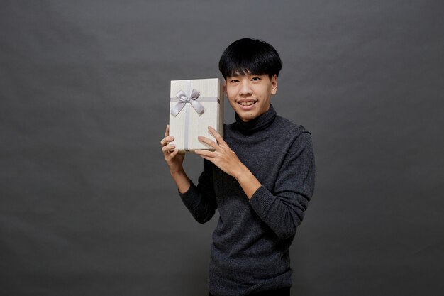 Concepto de fiesta y vacaciones de Navidad. Joven asiático con caja de regalo foto de estudio, aislado sobre fondo gris