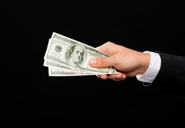 concepto de finanzas, personas, ahorros y pobreza - cierre de la mano masculina sosteniendo dinero en efectivo en dólares sobre fondo negro