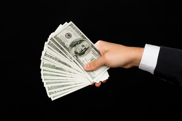 concepto de finanzas, personas, ahorros y riqueza - cierre de manos masculinas con dinero en efectivo en dólares sobre fondo negro