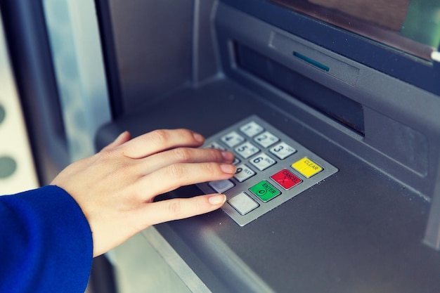 concepto de finanzas, tecnología, dinero y personas: cierre de la mano ingresando el código PIN en el cajero automático