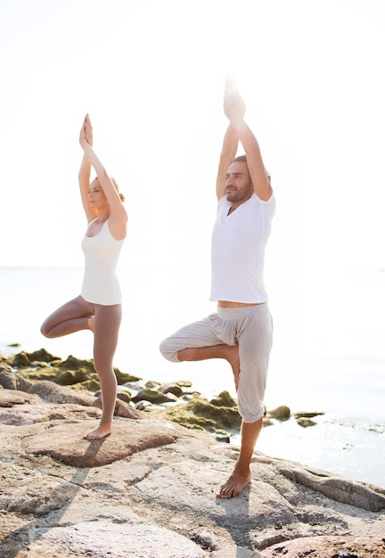 concepto de fitness, deporte, amistad y estilo de vida - pareja haciendo ejercicios de yoga en la playa