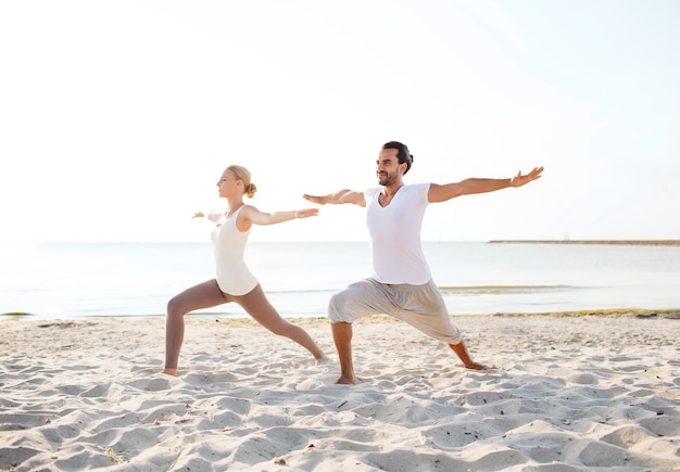 concepto de fitness, deporte, amistad y estilo de vida - pareja haciendo ejercicios de yoga en la playa