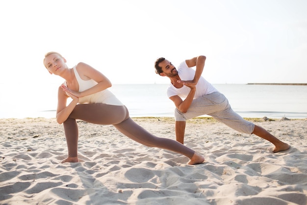 concepto de fitness, deporte, amistad y estilo de vida - pareja haciendo ejercicios de yoga en la playa