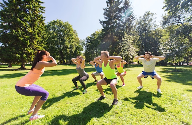 concepto de fitness, deporte, amistad y estilo de vida saludable - grupo de amigos adolescentes felices haciendo ejercicio y haciendo sentadillas en el campo de entrenamiento