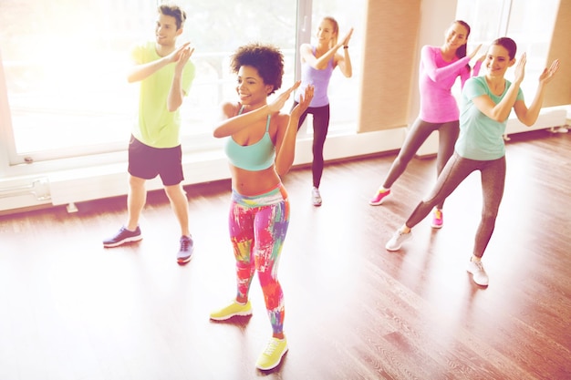 concepto de fitness, deporte, danza y estilo de vida - grupo de gente sonriente con entrenador bailando en el gimnasio o en el estudio