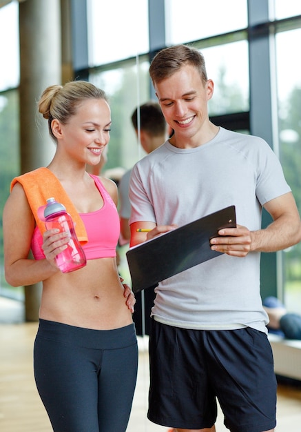 concepto de fitness, deporte, ejercicio y dieta - mujer joven sonriente con entrenador personal después de entrenar en el gimnasio