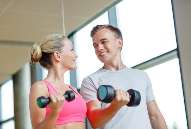concepto de fitness, deporte, ejercicio y dieta - mujer joven sonriente y entrenadora personal con pesas en el gimnasio