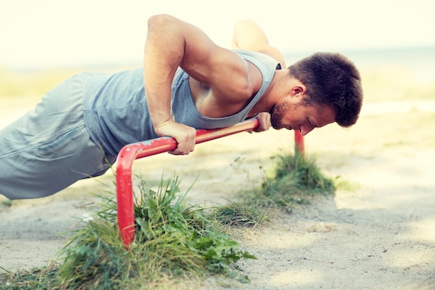 concepto de fitness, deporte, ejercicio, entrenamiento y estilo de vida - joven haciendo flexiones en la barra horizontal al aire libre