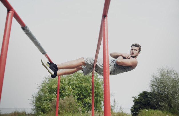 concepto de fitness, deporte, ejercicio, entrenamiento y estilo de vida - joven sentado en bares paralelos en el parque de verano