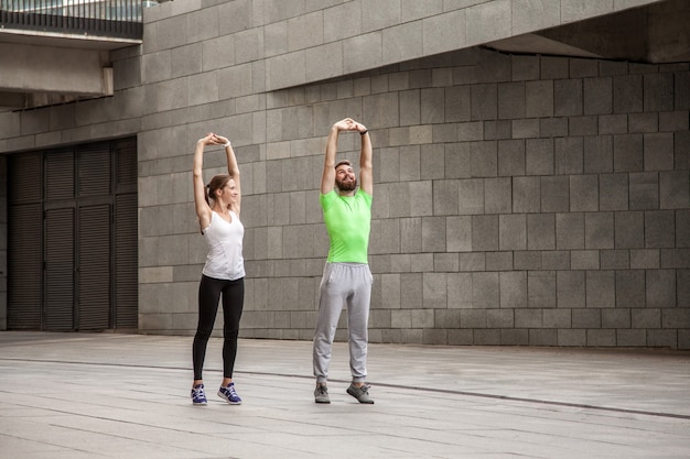 Concepto de fitness, deporte, ejercicio, entrenamiento y personas - pareja haciendo ejercicio de inmersión de tríceps en el banco de la calle de la ciudad.