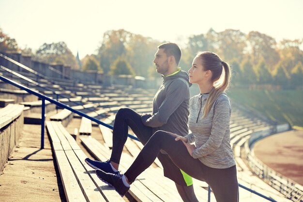 concepto de fitness, deporte, ejercicio y estilo de vida - pareja estirando la pierna en las gradas del estadio