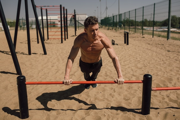 Concepto de fitness, deporte, entrenamiento y estilo de vida - joven haciendo ejercicio en barra horizontal en la playa. Foto de alta calidad