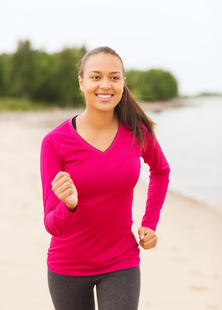 concepto de fitness, deporte, entrenamiento y estilo de vida - mujer afroamericana sonriente corriendo en pista al aire libre