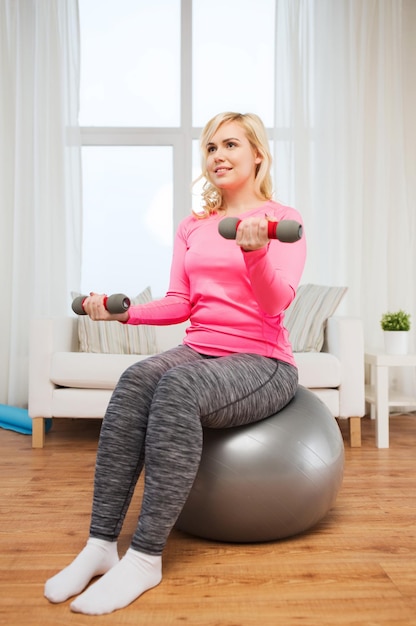 concepto de fitness, deporte, entrenamiento y estilo de vida - mujer sonriente con pesas y ejercicio de pelota en casa