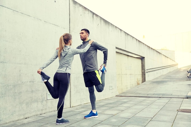 concepto de fitness, deporte, entrenamiento y estilo de vida - pareja de deportistas estirando la pierna en la calle de la ciudad