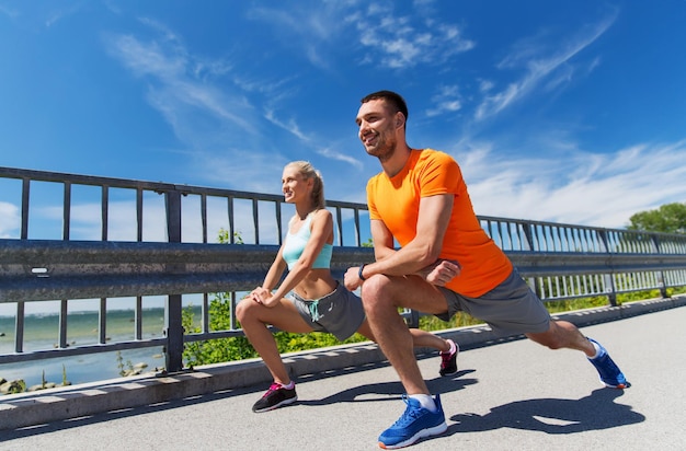 concepto de fitness, deporte, entrenamiento y estilo de vida - pareja sonriente estirando al aire libre