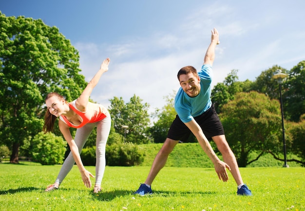 concepto de fitness, deporte, entrenamiento y estilo de vida - pareja sonriente estirando al aire libre