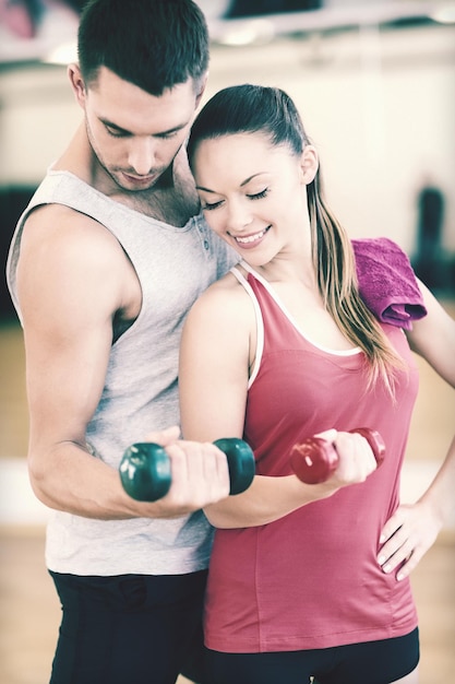 concepto de fitness, deporte, entrenamiento, gimnasio y estilo de vida: dos personas sonrientes que se ejercitan con pesas en el gimnasio